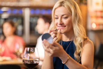 beauty, make up and people concept - smiling middle aged woman with lipstick and mirror applying makeup at restaurant. woman with lipstick applying make up at restaurant