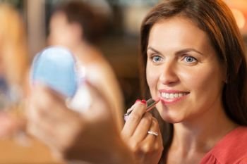 beauty, make up and people concept - close up of smiling middle aged woman with lipstick and mirror applying makeup. close up of woman with lipstick applying makeup