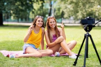 blogging, technology and leisure concept - teenage girls, friends or bloggers recording video by camera in summer park pointing finger up. teenage bloggers recording video by camera in park