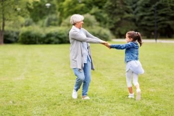 family, leisure and people concept - happy grandmother and granddaughter playing game or dancing at summer park. grandmother and granddaughter playing at park