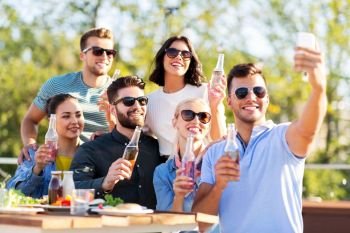 leisure and people concept - happy friends with non alcoholic drinks having dinner party on rooftop in summer and taking selfie by smartphone. happy friends taking selfie at rooftop party