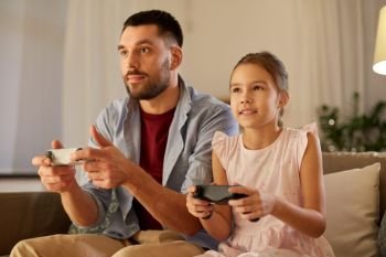 family, gaming and entertainment concept - happy father and little daughter with gamepads playing video game at home in evening. father and daughter playing video game at home