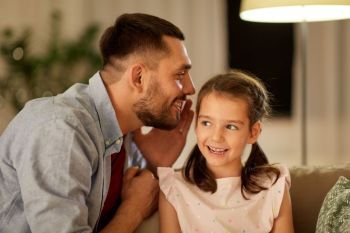 family, fatherhood, leisure and people concept - happy father whispering secret to daughter at home in evening. happy father whispering secret to daughter at home