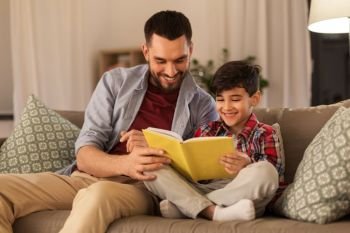family, childhood, fatherhood, leisure and people concept - happy smiling father and little son reading book on sofa at home. happy father and son reading book sofa at home