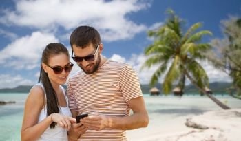 travel, tourism and technology concept - happy couple with smartphone in summer over tropical beach background in french polynesia. happy couple with smartphone in summer
