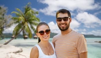 travel, tourism and people concept - happy couple in sunglasses outdoors in summer over tropical beach background in french polynesia. happy couple in sunglasses outdoors in summer