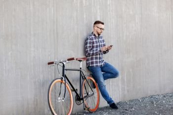 technology, leisure and lifestyle- happy young hipster man in earphones with smartphone and fixed gear bike listening to music on city street. hipster man in earphones with smartphone and bike
