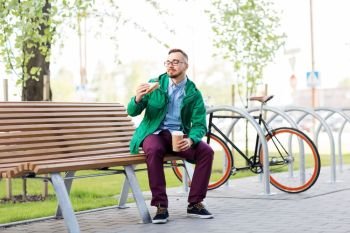 people, food and lifestyle - happy young man or hipster eating sandwich with takeaway coffee on city street. young man or hipster with coffee eating sandwich
