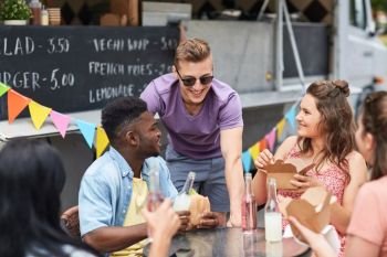 leisure and people concept - happy friends with drinks eating and talking at food truck. happy friends with drinks eating at food truck