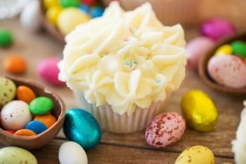easter, food and sweets concept - frosted cupcakes with chocolate eggs and candies on table. cupcake with chocolate eggs and candies on table