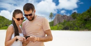 travel, tourism and technology concept - happy couple with smartphone over tropical beach on seychelles island background. happy couple with smartphone on seychelles island