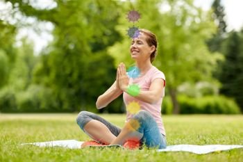 fitness, yoga and healthy lifestyle concept - happy woman meditating in summer park with seven chakra symbols. happy woman meditating in summer park
