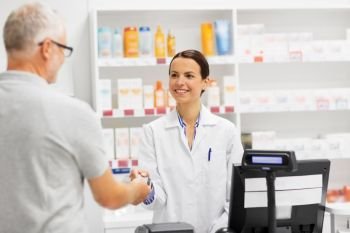 medicine, pharmaceutics, healthcare and people concept - happy smiling female apothecary taking senior customer credit card at pharmacy cash register. apothecary taking customer credit card at pharmacy