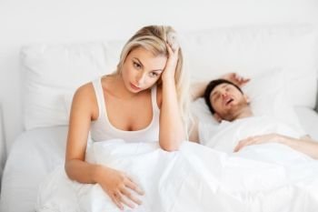 sleeping problems and people concept - unhappy woman lying in bed with snoring man. unhappy woman in bed with snoring sleeping man