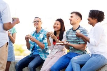 people, friendship and international concept - group of happy friends drinking juice, eating pizza and sandwiches and talking in park. friends eating pizza and sandwiches in park