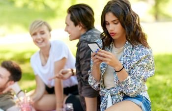 leisure, technology and people concept - woman using smartphone at picnic with friends in summer park. woman using smartphone at picnic with friends