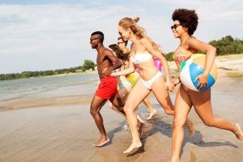 friendship, summer holidays and swimming concept - happy friends with floating mattress and inflatable ball running on beach. friends run with beach ball and swimming mattress