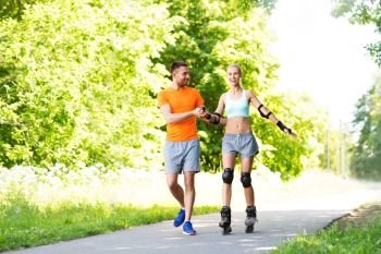 fitness, sport and healthy lifestyle concept - happy couple with roller skates riding outdoors in summer park. couple with roller skates riding in summer park