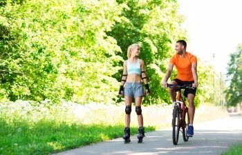 fitness, sport and healthy lifestyle concept - happy couple with rollerblades and bicycle riding in summer park. happy couple with rollerblades and bicycle riding