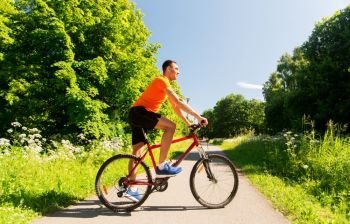 fitness, sport and healthy lifestyle concept - happy young man cycling by bicycle outdoors in summer park. happy young man cycling by bicycle in summer park