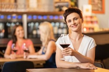 people, celebration and lifestyle concept - happy middle aged woman drinking red wine and talking at restaurant or bar. happy woman drinking red wine at bar or restaurant