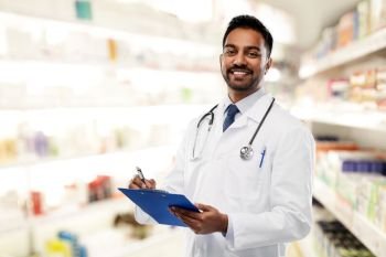 medicine, pharmacy and healthcare concept - smiling indian male doctor or pharmacist in white coat with stethoscope and clipboard over drugstore background. indian male doctor with clipboard and stethoscope