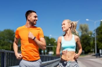 sport, technology and lifestyle concept - happy couple with fitness trackers running along bridge in summer. couple with fitness trackers running along bridge