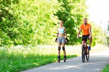 fitness, sport and healthy lifestyle concept - happy couple with rollerblades and bicycle riding in summer park. happy couple with rollerblades and bicycle riding