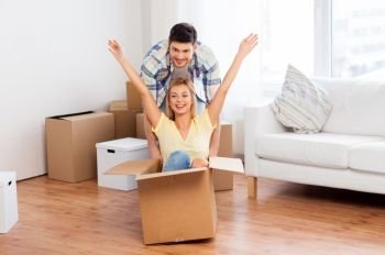 home, people, moving and real estate concept - happy couple having fun and riding in cardboard box at new home. happy couple having fun with boxes at new home