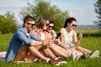 friendship, technology and leisure concept - group of smiling friends with smartphones sitting on grass in summer. smiling friends with smartphones sitting on grass