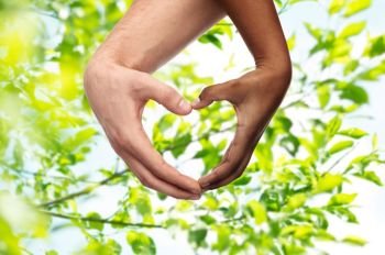 charity, love and diversity concept - close up of female and male hands of different skin color making heart shape over green natural background. hands of different skin color making heart shape