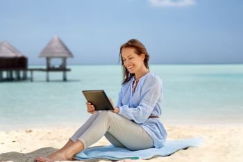 technology, people and leisure concept - happy smiling woman with tablet pc computer over tropical beach and bungalow on maldives background. happy smiling woman with tablet pc on summer beach