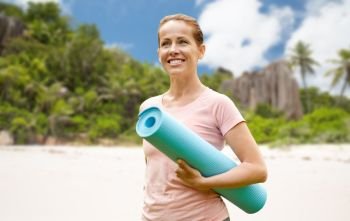 fitness, sport and healthy lifestyle concept - happy smiling woman with exercise mat over tropical beach on seychelles island background. happy smiling woman with exercise mat over beach