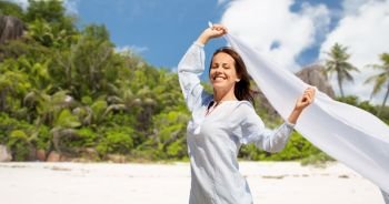 people and leisure concept - happy woman with shawl waving in wind over tropical beach on seychelles island background. happy woman with shawl waving in wind on beach