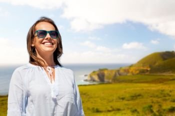 people and leisure concept - happy smiling woman in sunglasses over big sur coast of california background. smiling woman in sunglasses over big sur coast
