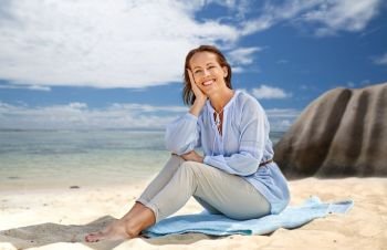people and summer concept - happy smiling woman sitting on towel over seychelles island tropical beach background. happy woman over seychelles island tropical beach