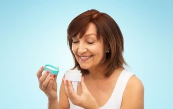 beauty, skincare and cosmetics concept - smiling senior woman with cream jar over blue background. smiling senior woman with cream jar