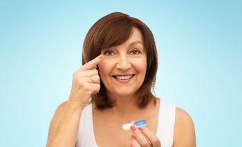 health, vision and old people concept - happy smiling senior woman putting on contact lenses over blue background. happy senior woman applying contact lenses