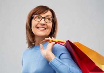 sale and old people concept - smiling senior woman in glasses with shopping bags over grey background. senior woman with shopping bags over grey