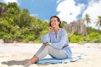 summer, people and leisure concept - happy smiling woman sitting over tropical beach on seychelles island background. happy woman sitting on summer beach on seychelles