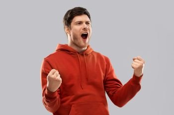 success, winning and people concept - happy young man celebrating triumph and making fist pump gesture over grey background. happy man celebrating and making fist pump gesture