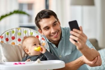 family, fatherhood and people concept - father with little baby daughter in highchair taking selfie by smartphone at home. father with baby daughter taking selfie at home