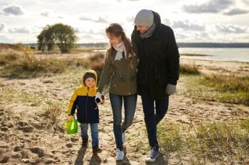 family, leisure and people concept - happy mother, father and little son with sand toy kit walking along autumn beach. happy family walking along autumn beach