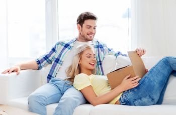 people, delivery, shipping and postal service concept - happy couple opening cardboard box or parcel at home. happy couple opening parcel box at home