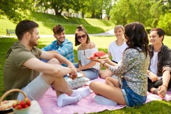 friendship, leisure and summer concept - group of happy friends eating watermelon at picnic in park. happy friends eating watermelon at summer picnic