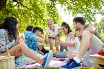 friendship and leisure concept - group of happy friends with non alcoholic drinks and food at picnic in summer park. friends with drinks and food at picnic in park