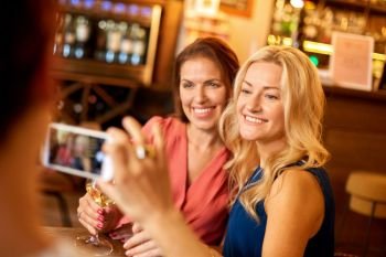 people, technology and lifestyle concept - woman photographing friends by smartphone at wine bar or restaurant. woman picturing friends by smartphone at wine bar