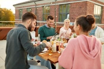 leisure and people concept - happy friends eating at dinner party on rooftop in summer. friends having dinner or rooftop party in summer