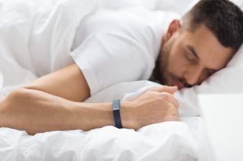people, technology and rest concept - close up of man with activity tracker sleeping in bed. close up of man sleeping with activity tracker