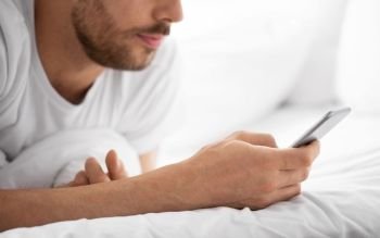 technology, communication and people concept - close up of young man texting on smartphone in bed at home in morning. close up of man with smartphone in bed in morning